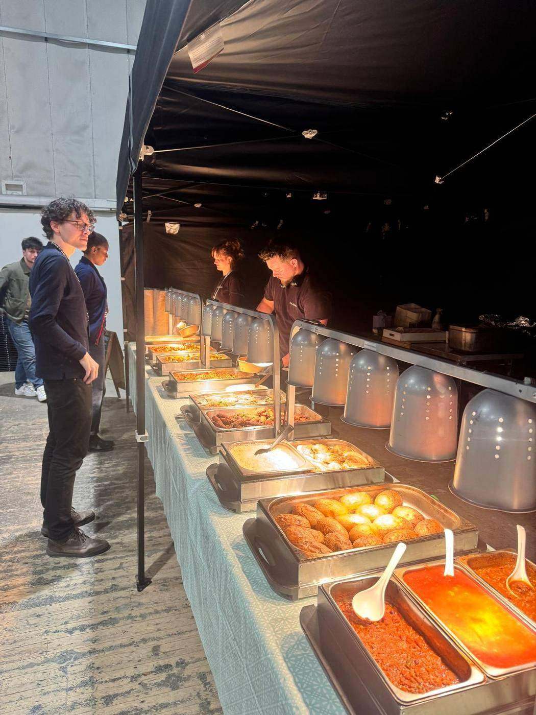 Crew queuing at a hot buffet line inside a location marquee